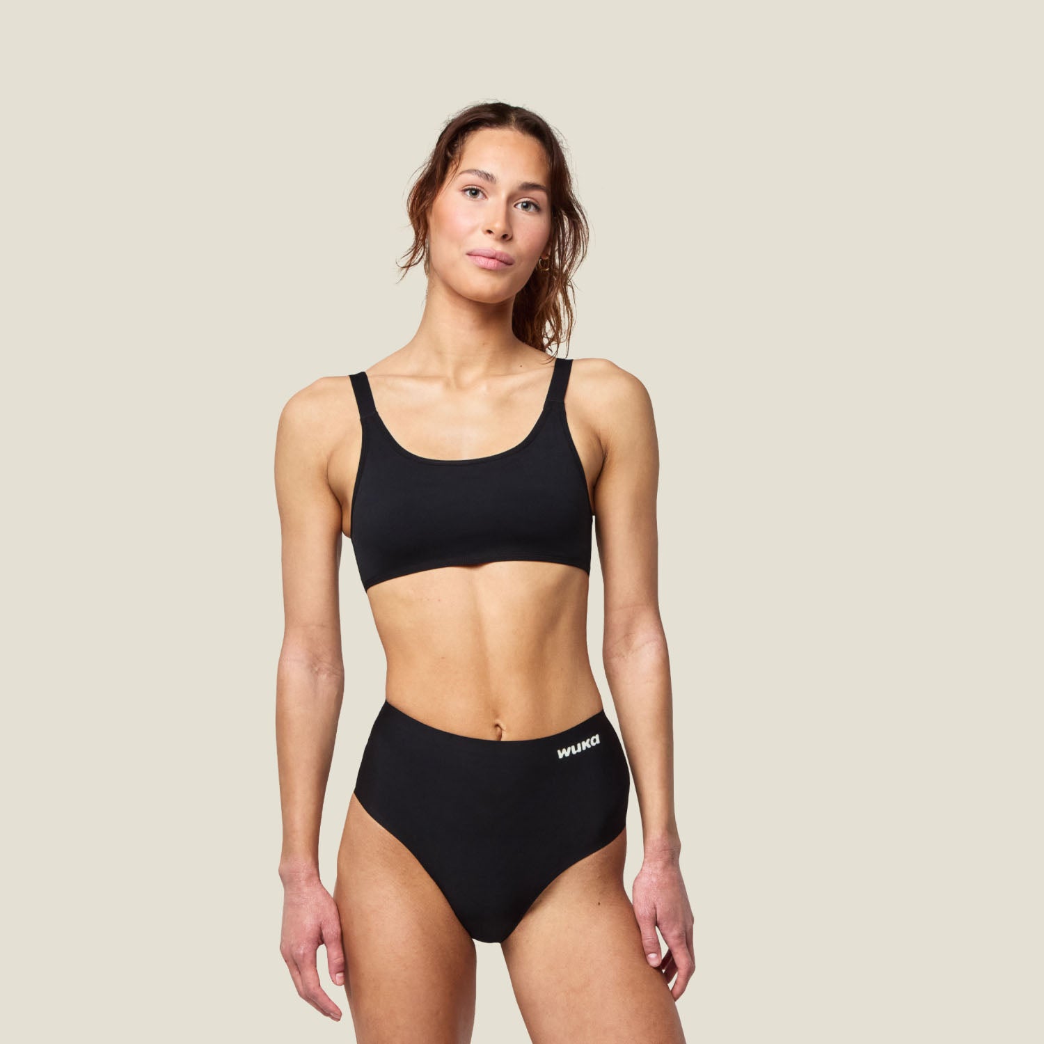 Adult woman wearing WUKA Stretch Seamless Midi Brief in black for light flow, shown full-body to highlight fit and comfort.