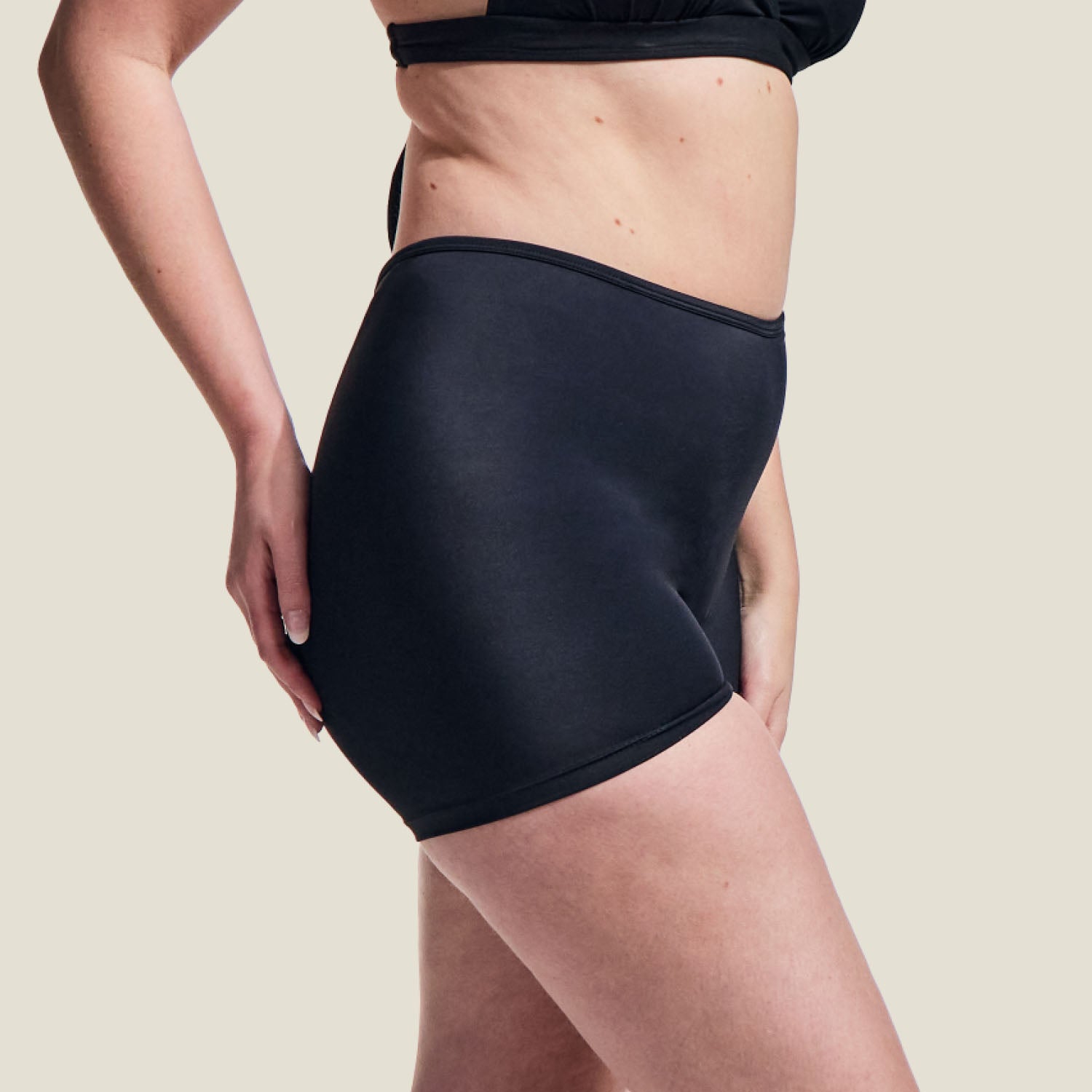 Side profile of WUKA period swim shorts in black, medium flow, showing body-contouring fit and smooth stitching.