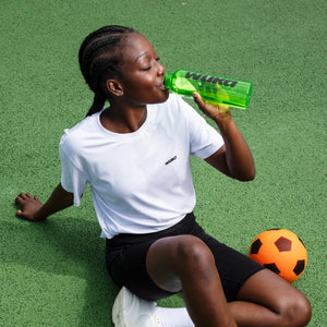 Young athlete drinking from a WUKA water bottle on a sports court, highlighting hydration and self-care while playing sport on her period